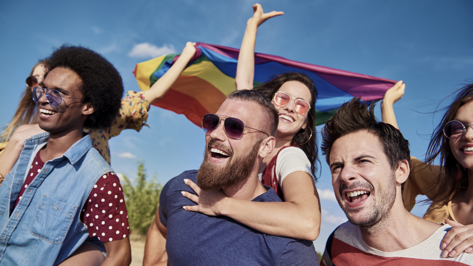 A grouple of people on beach with a gay pride flag flying behind them