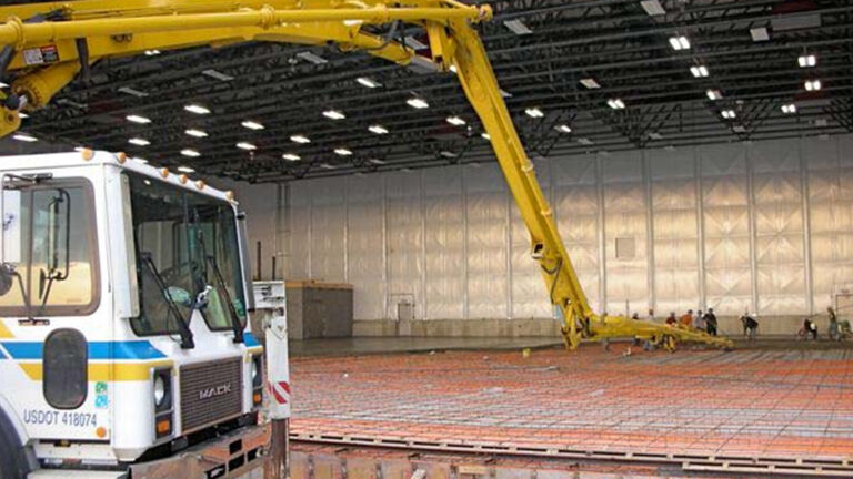 Machines operating to assemble heated flooring in airport hangar.