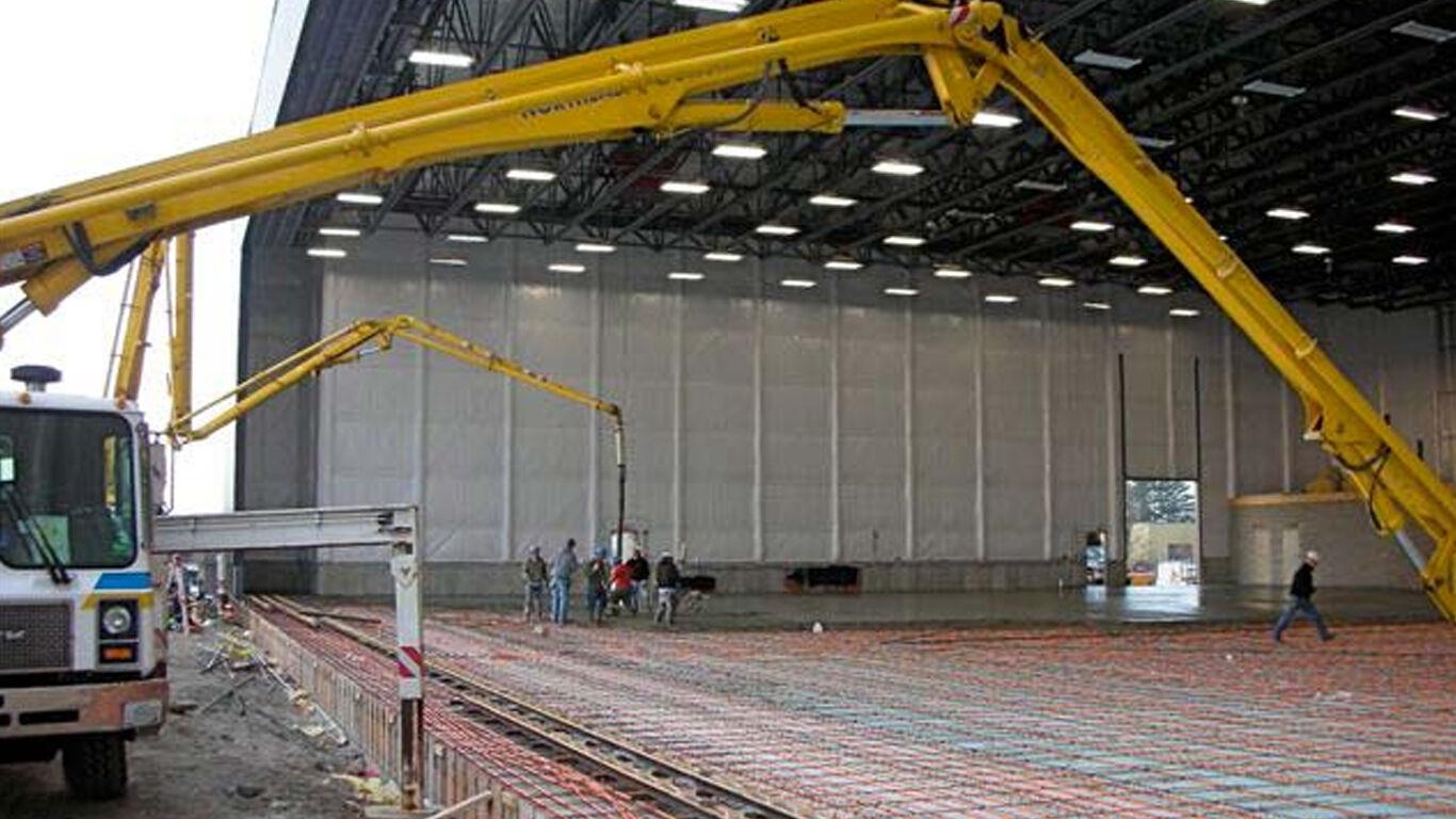 Machines operating to assemble heated flooring in airport hangar.